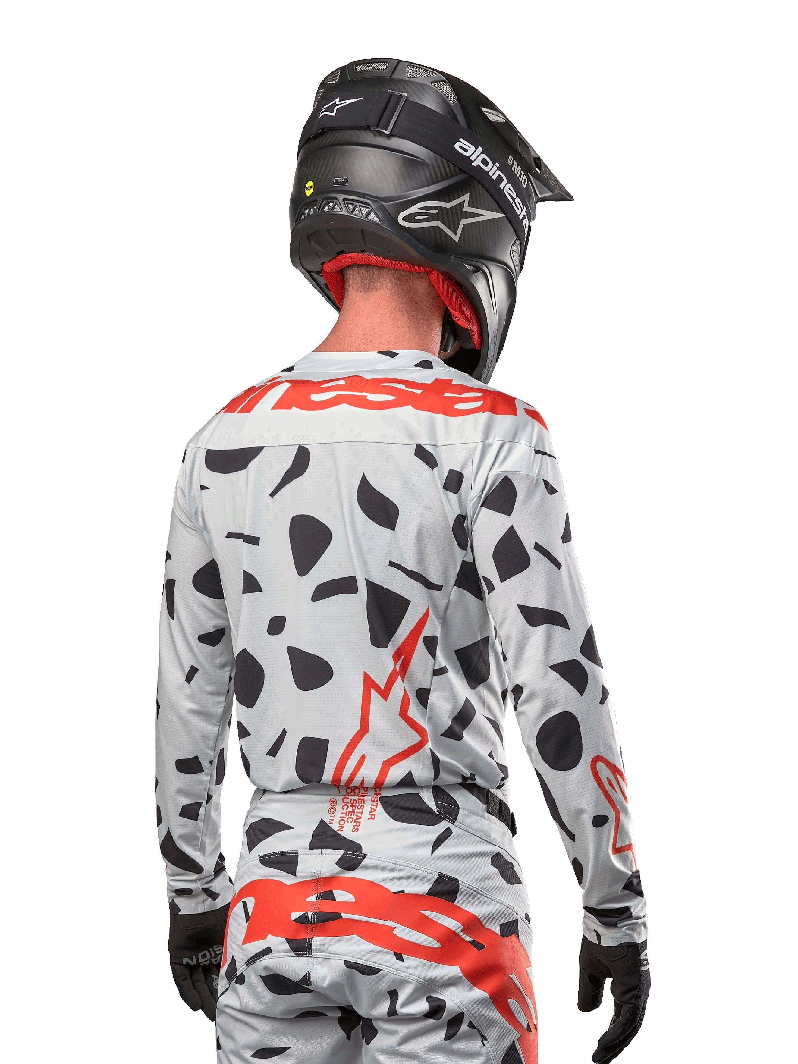 Motocyklista motocrossowy widziany od tyłu w koszulce Alpinestars 2024 Techstar Rantera w kolorze Haze Gray Camo, charakteryzującej się jasnoszarą bazą z czarnymi graficznymi wzorami oraz wyrazistym czerwonym logo Alpinestars na plecach i ramionach, w zestawie z pasującymi spodniami i czarnym kaskiem.