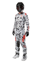 Alpinestars Techstar Rantera Pants 2024, spodnie motocrossowe, Haze Gray Camo, noszone z dopasowaną bluzą, czarnym kaskiem oraz biało-czarnymi butami, z czarnymi abstrakcyjnymi wzorami i czerwonymi akcentami, kompletny strój wyścigowy off-road