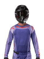 Koszulka Alpinestars 2024 Techstar Ocuri, fioletowa i jaskrawopomarańczowa, noszona przez motocyklistę w czarnym kasku i goglach, laserowo wycinane perforacje na klatce piersiowej, atletyczny krój wyścigowy, wyrazisty czerwony branding na ramionach i klatce piersiowej.