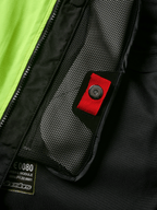 Alpinestars Tech-Air® 3 V2 System, zbliżenie na detal wewnętrznej kieszeni z siatki z czerwonym uchwytem i zatrzaskiem, jaskrawożółty panel fluo, czarna konstrukcja tekstylna z widoczną etykietą modułu poduszki powietrznej i zamkiem błyskawicznym