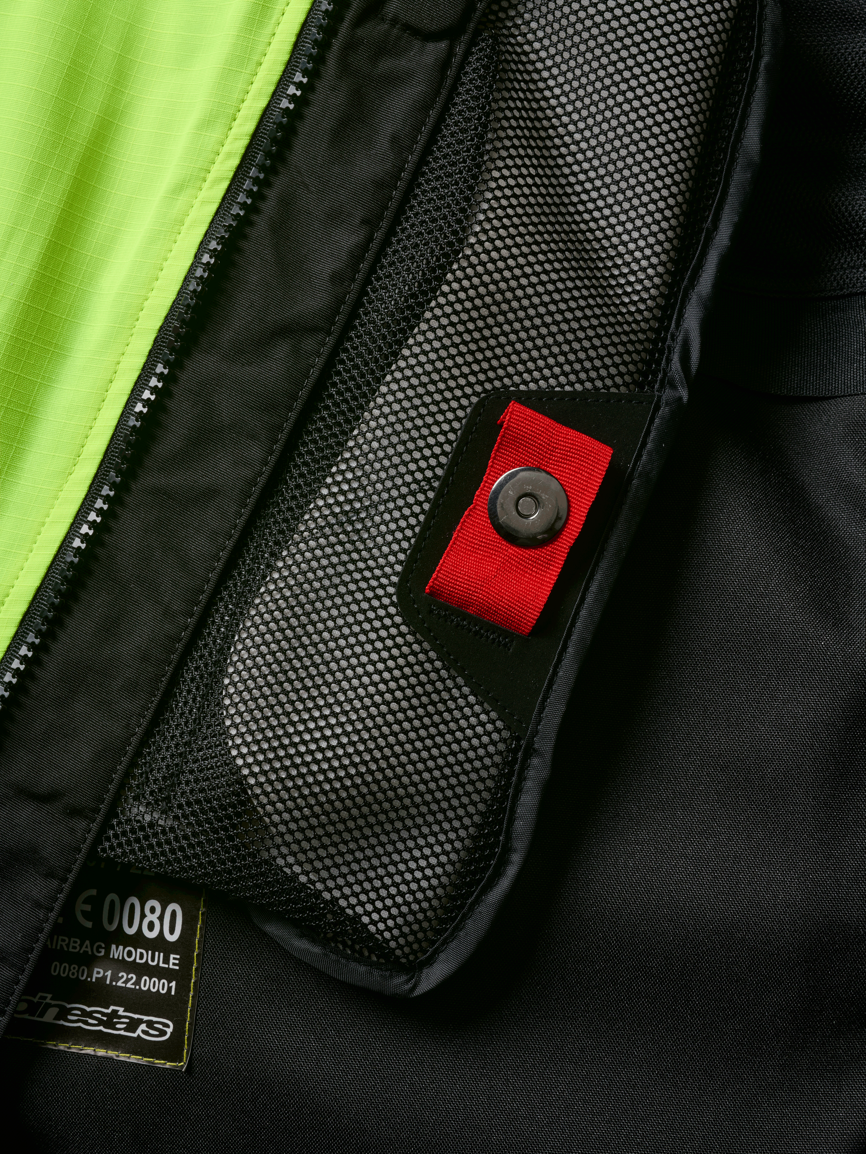 Alpinestars Tech-Air® 3 V2 System, zbliżenie na detal wewnętrznej kieszeni z siatki z czerwonym uchwytem i zatrzaskiem, jaskrawożółty panel fluo, czarna konstrukcja tekstylna z widoczną etykietą modułu poduszki powietrznej i zamkiem błyskawicznym