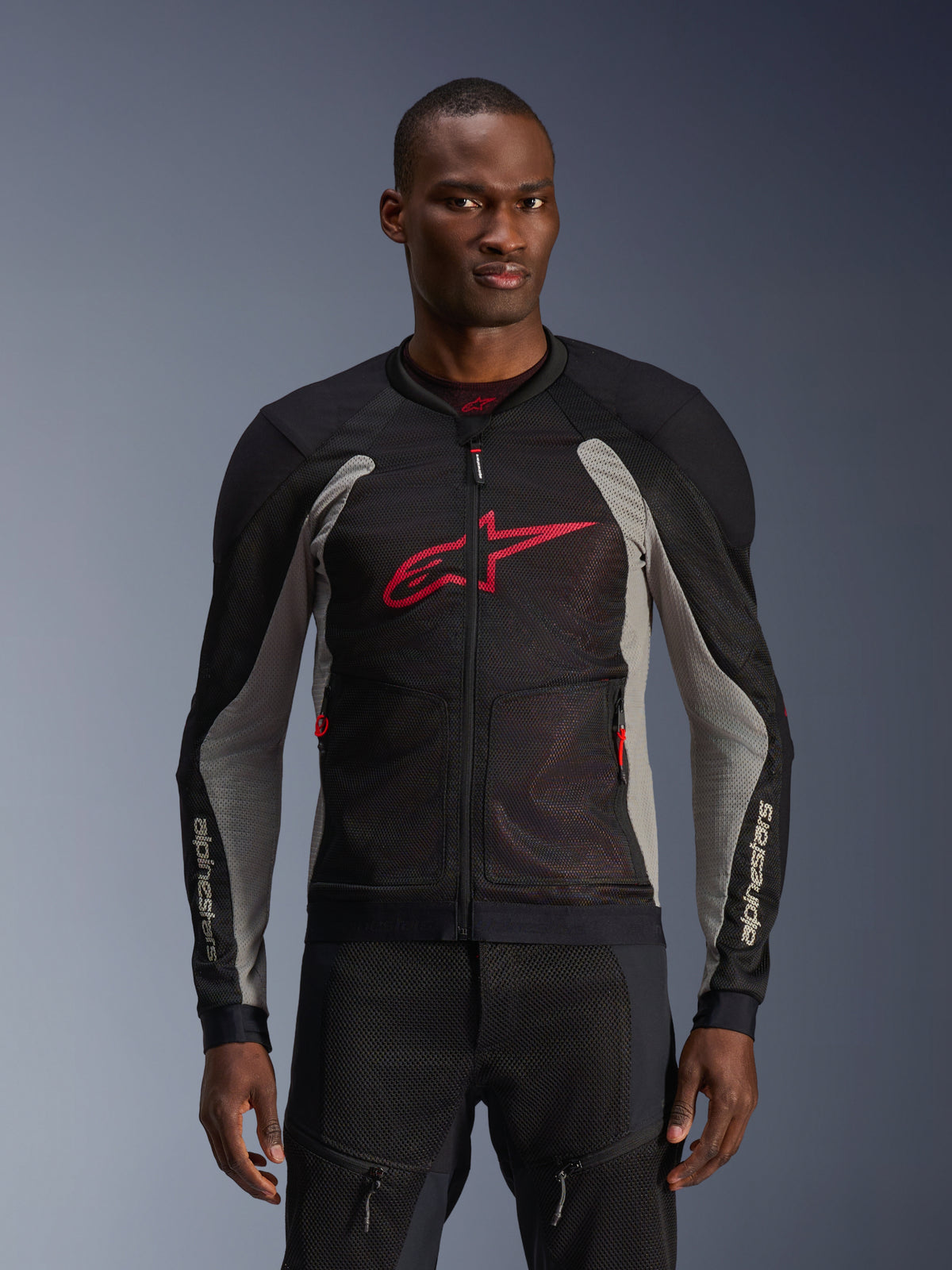Alpinestars Troop-Air Jacket, motocyklowa kurtka z panelami mesh, czarna i szara z jaskrawoczerwonymi akcentami, prezentowana przez modela, oddychające panele z siatki 2D, duże czerwone logo Astars na klatce piersiowej, techniczny sportowy design do jazdy miejskiej