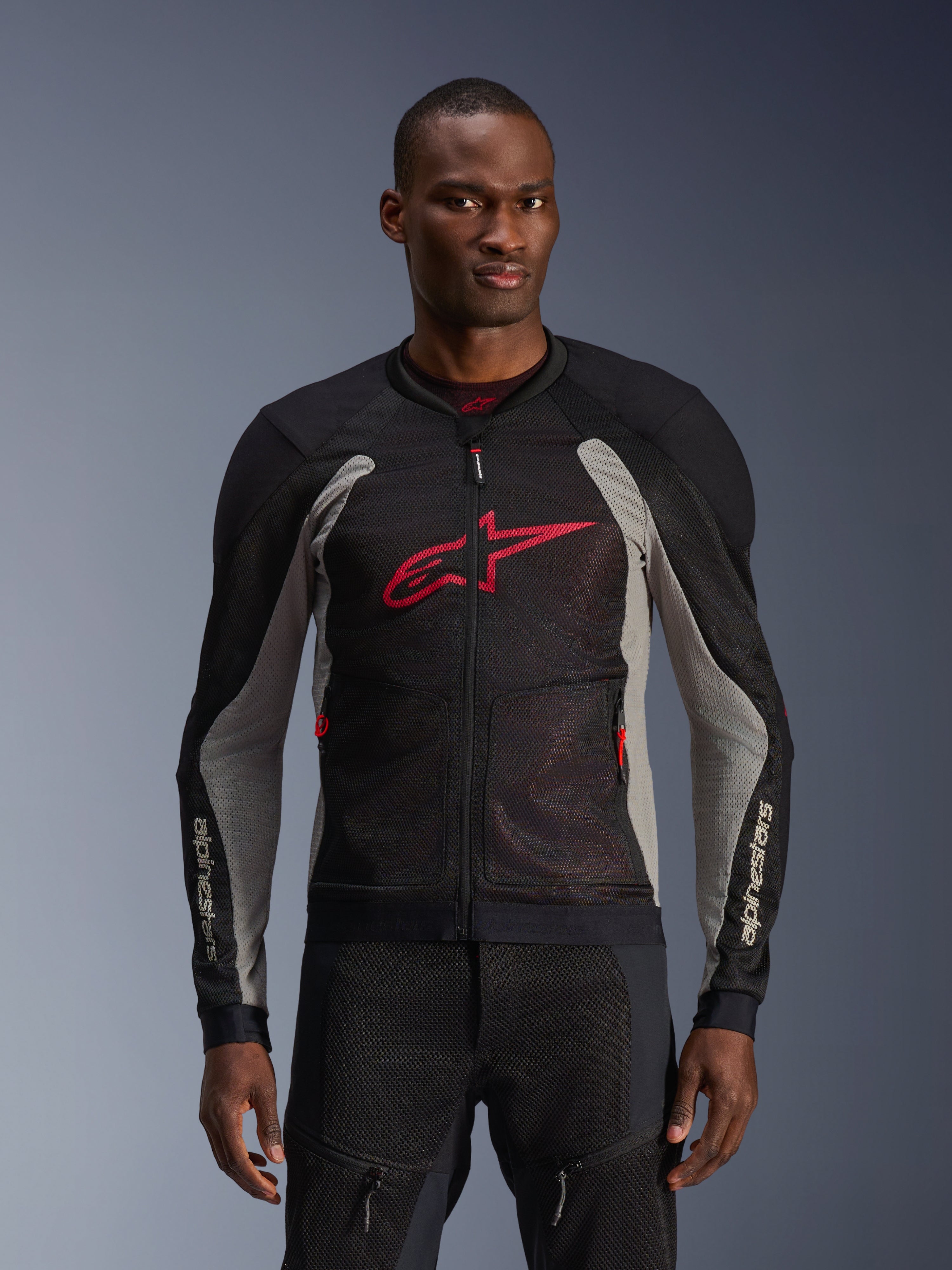 Alpinestars Troop-Air Jacket, motocyklowa kurtka z panelami mesh, czarna i szara z jaskrawoczerwonymi akcentami, prezentowana przez modela, oddychające panele z siatki 2D, duże czerwone logo Astars na klatce piersiowej, techniczny sportowy design do jazdy miejskiej