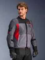 Alpinestars St-2 Air Jacket, kurtka motocyklowa, szara i ciemnoszara z jaskrawoczerwonymi akcentami, duże siatkowe panele wentylacyjne, laserowo perforowane detale, czerwone logo gwiazdy, prezentowana przez modela w studio, nowoczesny styl adventure touring
