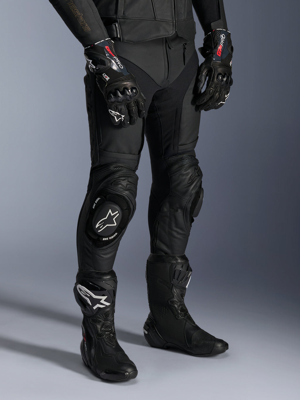 Alpinestars Missile V3 Leather Pants, czarne motocyklowe spodnie wyścigowe, noszone z pasującymi rękawicami GP Pro i technicznymi butami wyścigowymi, konstrukcja ze skóry premium ze sliderami kolan z białym logo, profesjonalna estetyka wyścigowa do użytku na torze i drodze