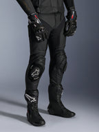 Alpinestars Missile V3 Leather Pants, czarne motocyklowe spodnie wyścigowe, noszone z pasującymi rękawicami GP Pro i technicznymi butami wyścigowymi, konstrukcja ze skóry premium ze sliderami kolan z białym logo, profesjonalna estetyka wyścigowa do użytku na torze i drodze