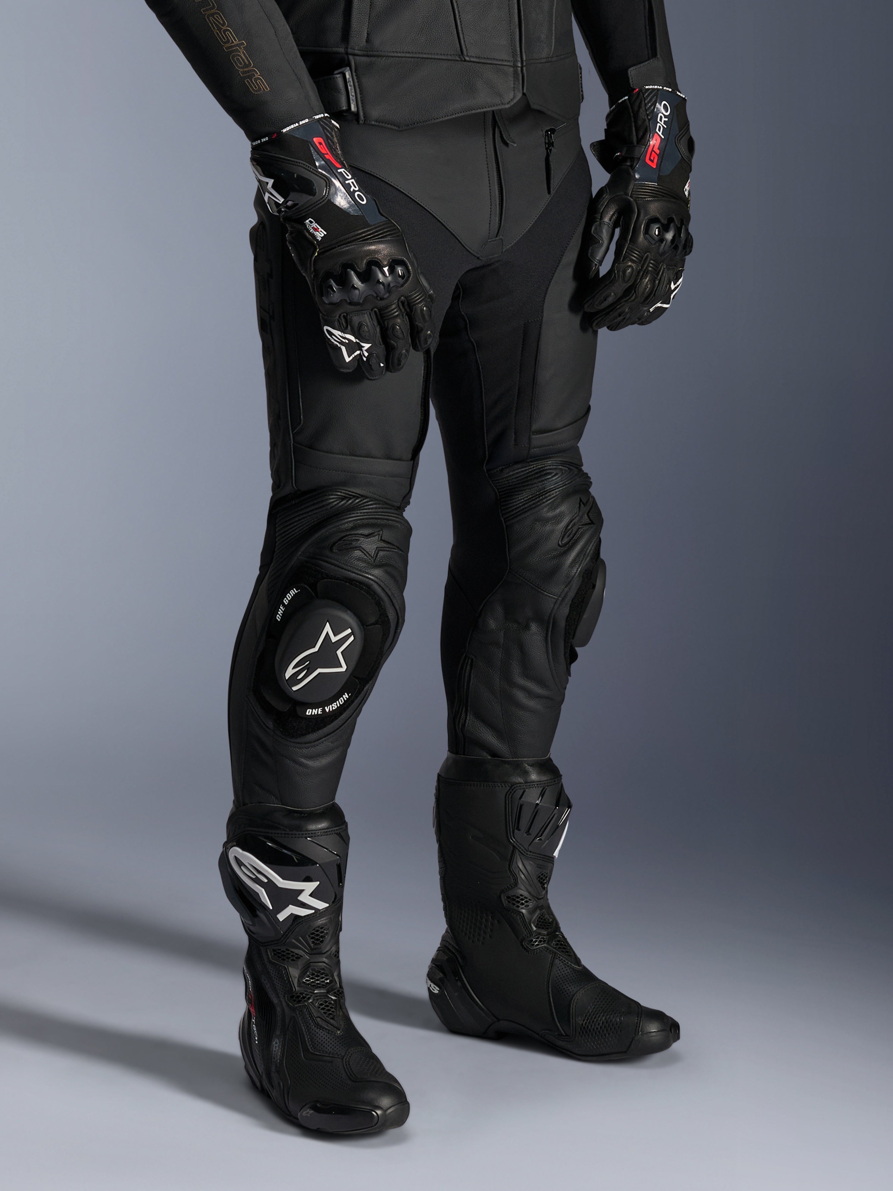 Alpinestars Missile V3 Leather Pants, czarne motocyklowe spodnie wyścigowe, noszone z pasującymi rękawicami GP Pro i technicznymi butami wyścigowymi, konstrukcja ze skóry premium ze sliderami kolan z białym logo, profesjonalna estetyka wyścigowa do użytku na torze i drodze