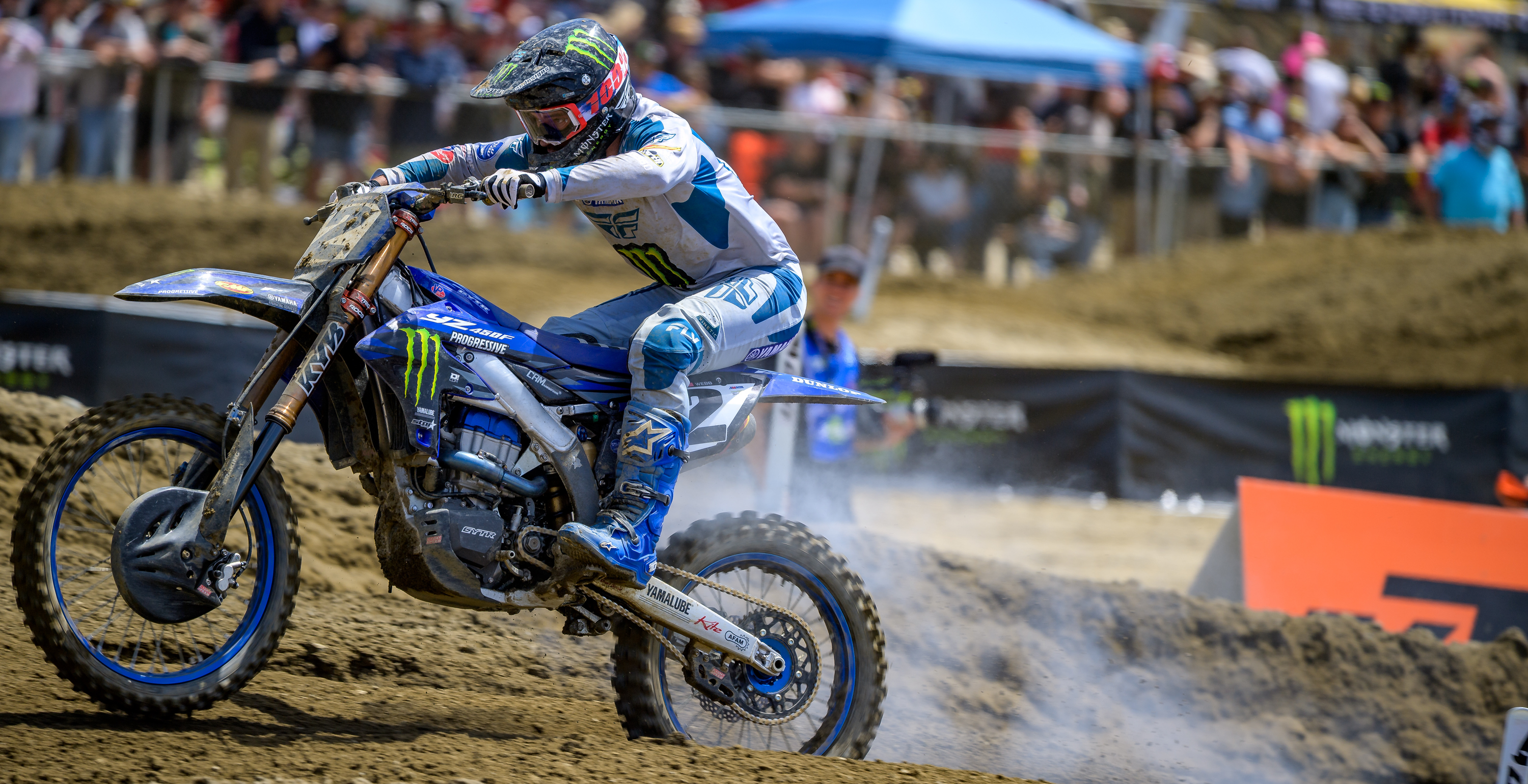 Motocross rider Cooper Webb on a dirt bike with Monster Energy branding on a muddy track.