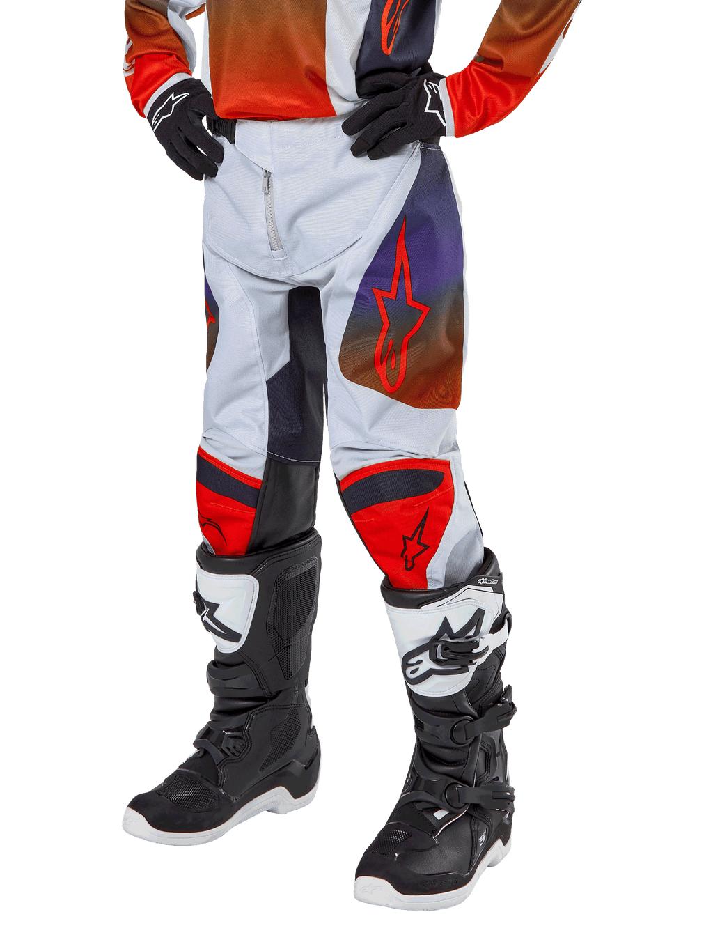 Alpinestars 2024 Youth Racer Hoen Pants, spodnie motocrossowe, jasnoszare z jaskrawopomarańczowymi i czarnymi akcentami, z czerwonym logo gwiazdy na udach i czerwonymi panelami na kolanach, noszone z czarno-białymi butami, wytrzymała konstrukcja do wyścigów terenowych