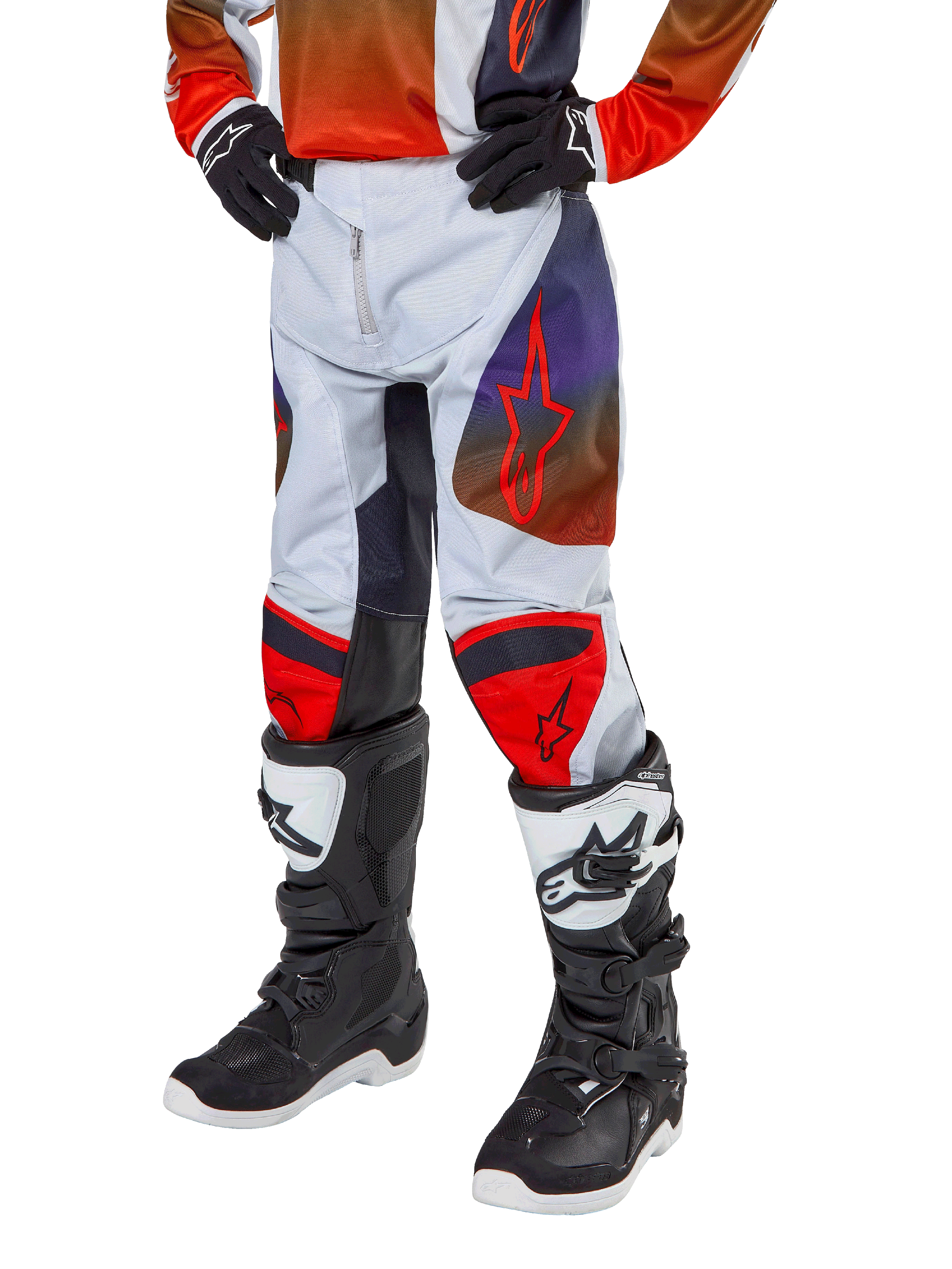 Alpinestars 2024 Youth Racer Hoen Pants, spodnie motocrossowe, jasnoszare z jaskrawopomarańczowymi i czarnymi akcentami, z czerwonym logo gwiazdy na udach i czerwonymi panelami na kolanach, noszone z czarno-białymi butami, wytrzymała konstrukcja do wyścigów terenowych
