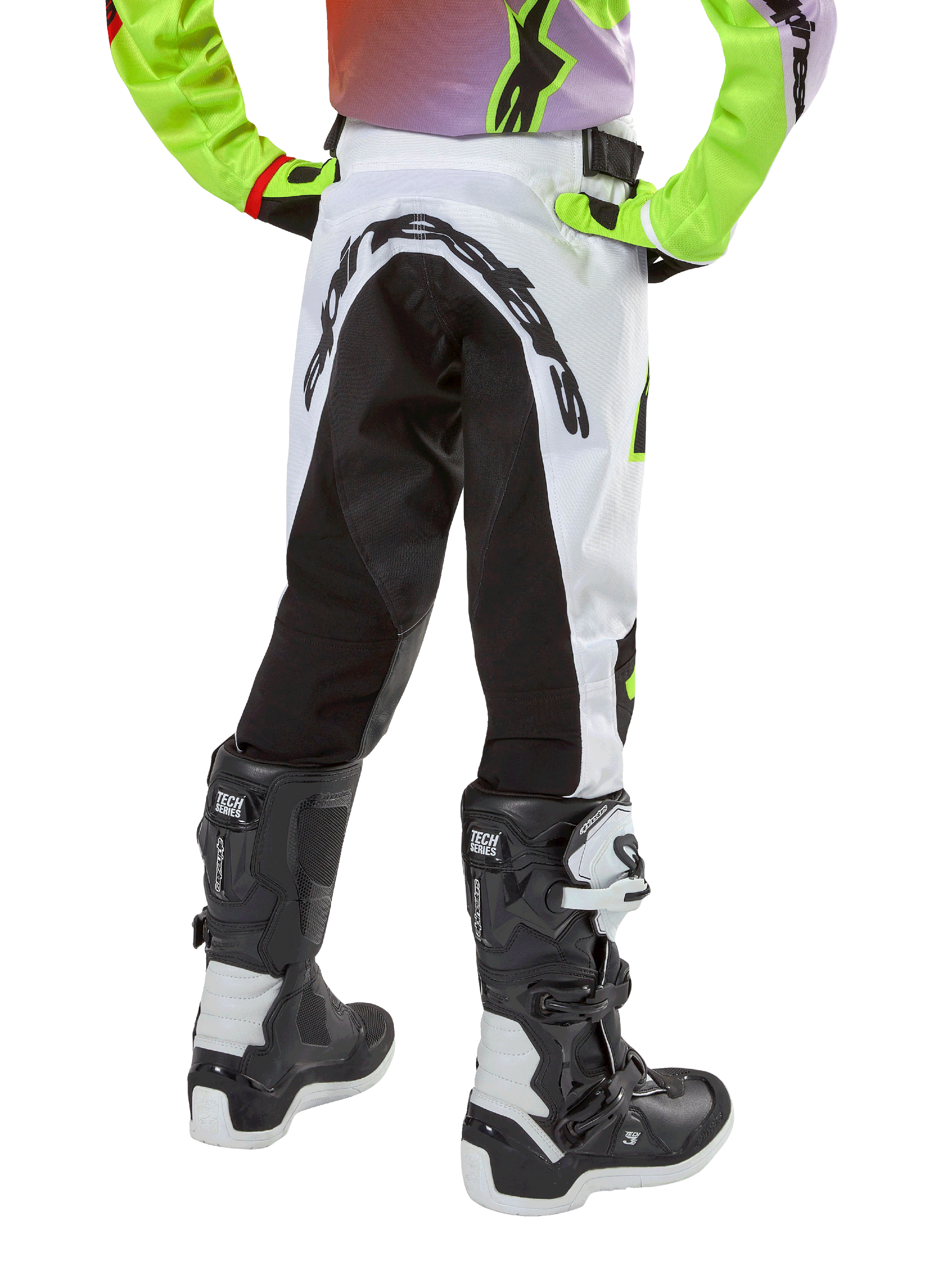 Alpinestars Youth 2024 Racer Lucent Pants, spodnie motocrossowe, biało-czarne z neonowymi akcentami, widok z tyłu ukazujący duży elastyczny panel oraz logo Alpinestars, noszone z czarno-białymi butami Alpinestars Tech Series