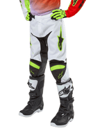 Alpinestars Youth 2024 Racer Lucent Pants, spodnie motocrossowe, białe, neonowo-czerwone i żółte fluo, widok na dolną część ciała z czarnymi elastycznymi panelami i neonowymi akcentami, noszone z czarno-białymi butami wyścigowymi i neonowo-żółtymi rękawicami, techniczna odzież terenowa dla młodzieży