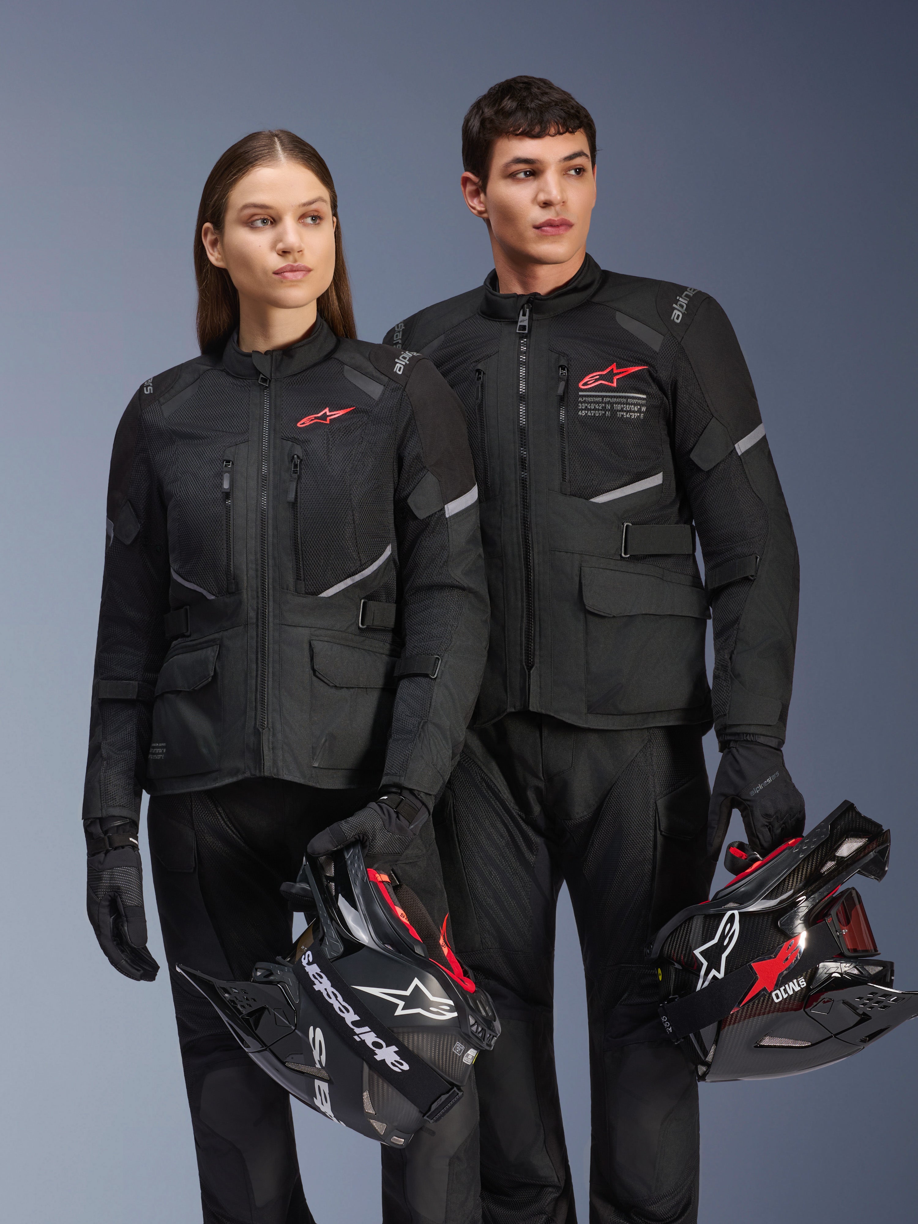 Mężczyzna i kobieta w kurtkach Alpinestars Andes Air Drystar®, czarna odzież adventure touring z panelami z siatki i odblaskowymi detalami, pasujące czarne spodnie i rękawice, trzymający kaski motocrossowe, zdjęcie studyjne profesjonalnej odzieży motocyklowej
