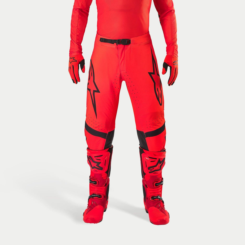 Alpinestars Supertech Ember LE Pants, spodnie motocrossowe, kolory czerwony fluo i jaskrawy czerwony z czarnymi akcentami, czarne logo gwiazdy na udach, czarna klamra w pasie i panele na kolanach, zestawione z dopasowanymi czerwonymi butami i rękawicami tworzącymi spójny strój wyścigowy