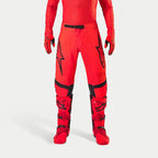 Alpinestars Supertech Ember LE Pants, spodnie motocrossowe, kolory czerwony fluo i jaskrawy czerwony z czarnymi akcentami, czarne logo gwiazdy na udach, czarna klamra w pasie i panele na kolanach, zestawione z dopasowanymi czerwonymi butami i rękawicami tworzącymi spójny strój wyścigowy