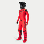 Motocyklista motocrossowy w kompletnym stroju wyścigowym, koszulka i spodnie Supertech Ember LE w kolorystyce Red Fluo i czarnej, czarny kask z goglami, pasujące czerwono-czarne buty i rękawice, profesjonalny zestaw do wyścigów off-road
